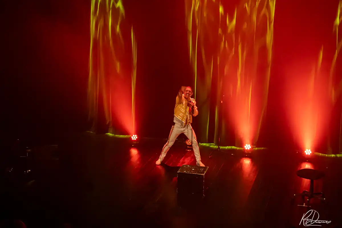 Je Vis avec Freddie Mercury – Jeux de lumière Thierry Margot en veste jaune sur la scène de L’Esty, entouré de puissants éclairages rouges et orangés.