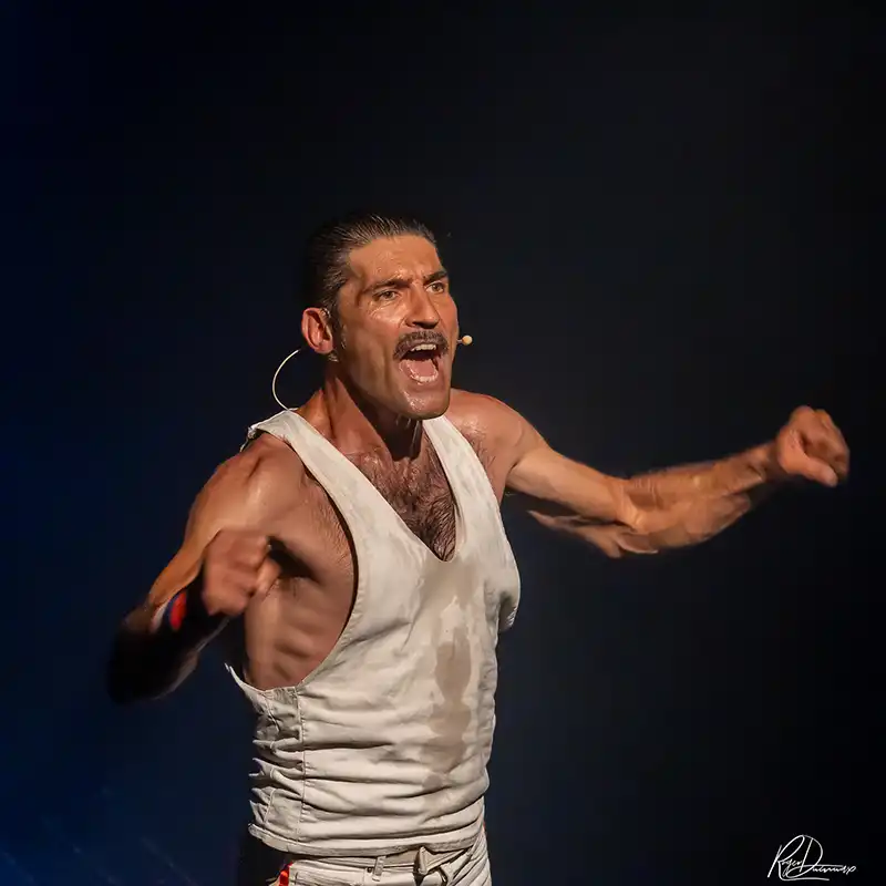 Thierry Margot – Je Vis avec Freddie Mercury Thierry Margot en débardeur blanc, les bras écartés, pendant le spectacle Je Vis avec Freddie Mercury à L’Esty.