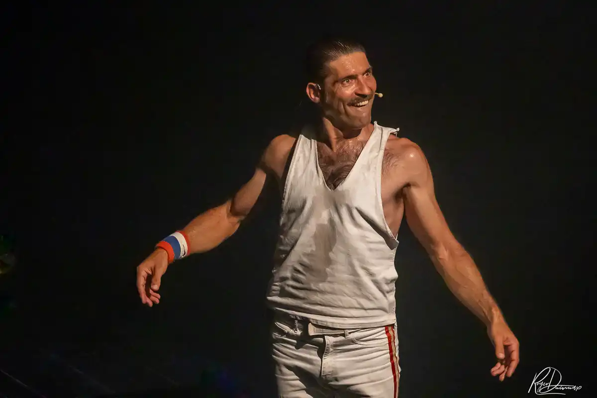 Thierry Margot – Un moment de complicité sur scène Thierry Margot souriant, en débardeur blanc, pendant sa représentation de Je Vis avec Freddie Mercury à Chavanod.